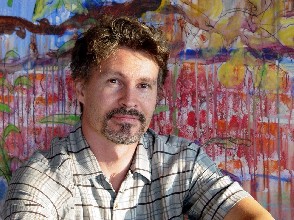 Kunstenaar Arnor Bieltvedt, geportretteerd op de voorgrond van één van zijn schilderijen. De kunstenaar schildert rechtstreeks vanuit het hart als een echte expressionist, maar is tegelijkertijd goed gewapend met ambachtelijke vakkennis. Bekijk zijn schilderijen.